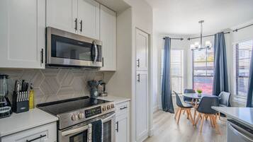 Een moderne keuken met een magnetron, fornuis en oven. Er is een eethoek met een tafel en stoelen.