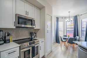 Een moderne keuken met een magnetron, fornuis en oven. Er is een eethoek met een tafel en stoelen.