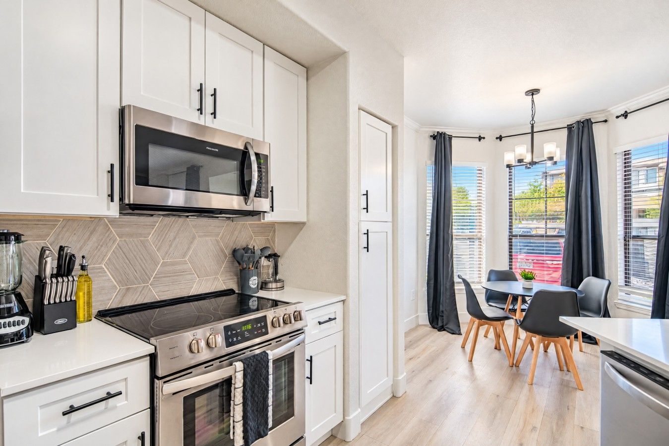 A modern kitchen with a microwave, stove, and oven. There is a dining area with a table and chairs.
