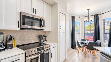 A modern kitchen with a microwave, stove, and oven. There is a dining area with a table and chairs.