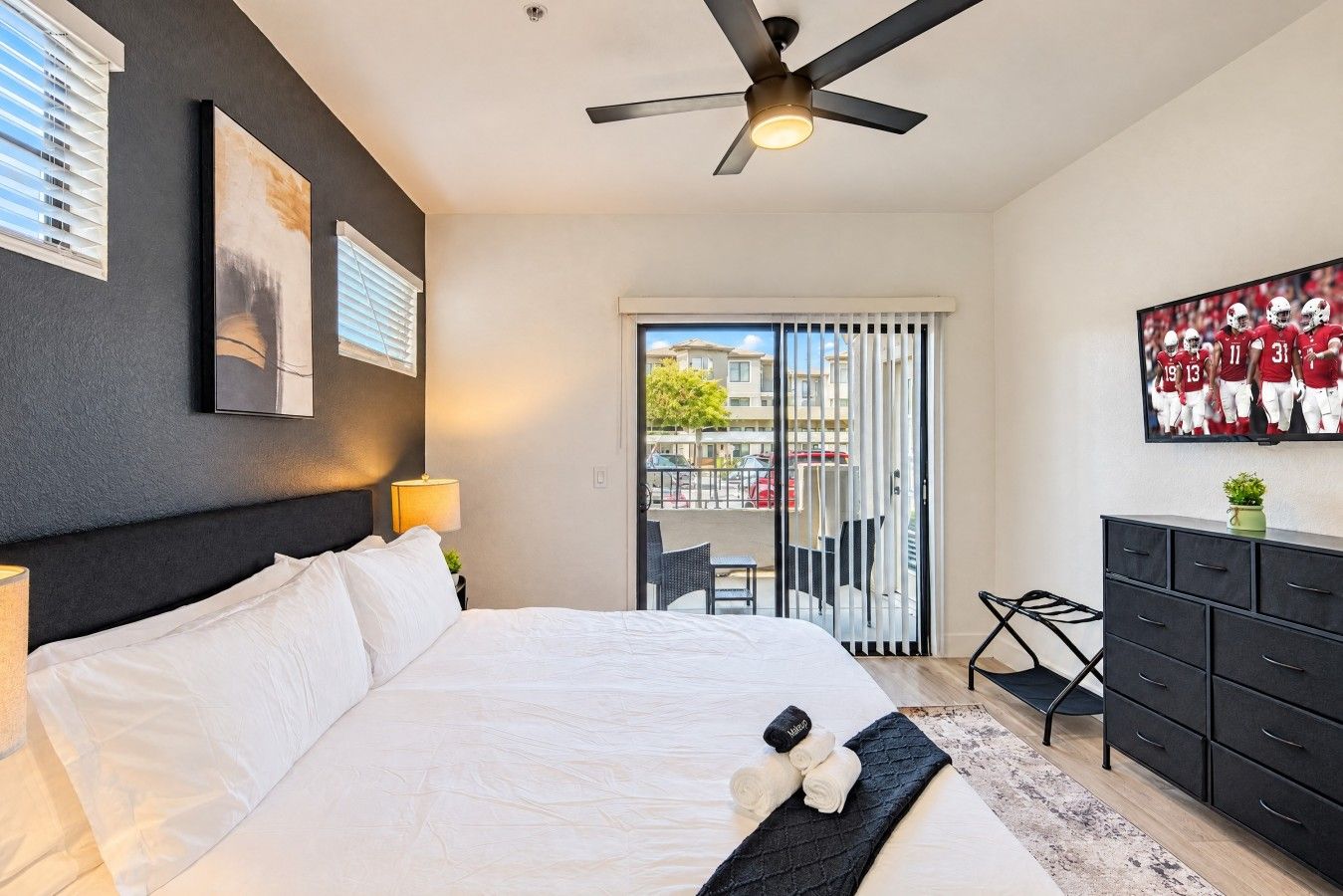 Une chambre d’hôtel avec un lit, un ventilateur de plafond, une télévision, une commode et un balcon offrant une vue sur la ville.