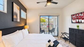 Une chambre d’hôtel avec un lit, un ventilateur de plafond, une télévision, une commode et un balcon offrant une vue sur la ville.