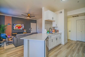 A modern kitchen with white cabinetry, a central island, and a dining area with a sofa and table.