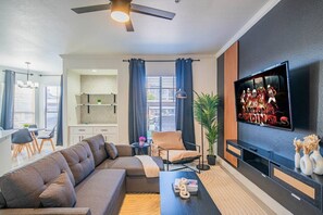 A modern living room with a sectional sofa, a coffee table, a TV mounted on the wall, and a dining area with a table and chairs. - Prime Location | Balcony, Pool, Gym, Parking, W/D (Glendale)