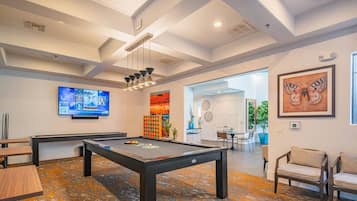 A pool table in a room with a patterned carpet, a television mounted on the wall, and a framed butterfly painting.