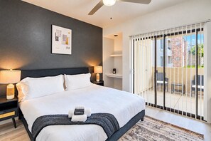 Una habitación de hotel moderna con una cama grande, dos mesitas de noche con lámparas, un ventilador de techo, vistas al balcón exterior y un cuadro en la pared.