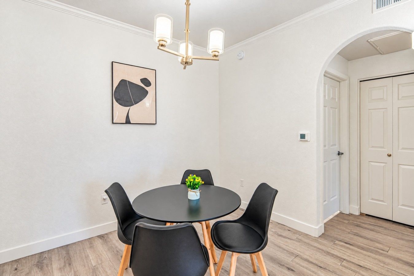 Un coin repas comprenant une table ronde, quatre chaises, un lustre et une œuvre d’art accrochée au mur.