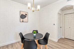 Un comedor con una mesa redonda, cuatro sillas, una araña y una obra de arte colgada en la pared.