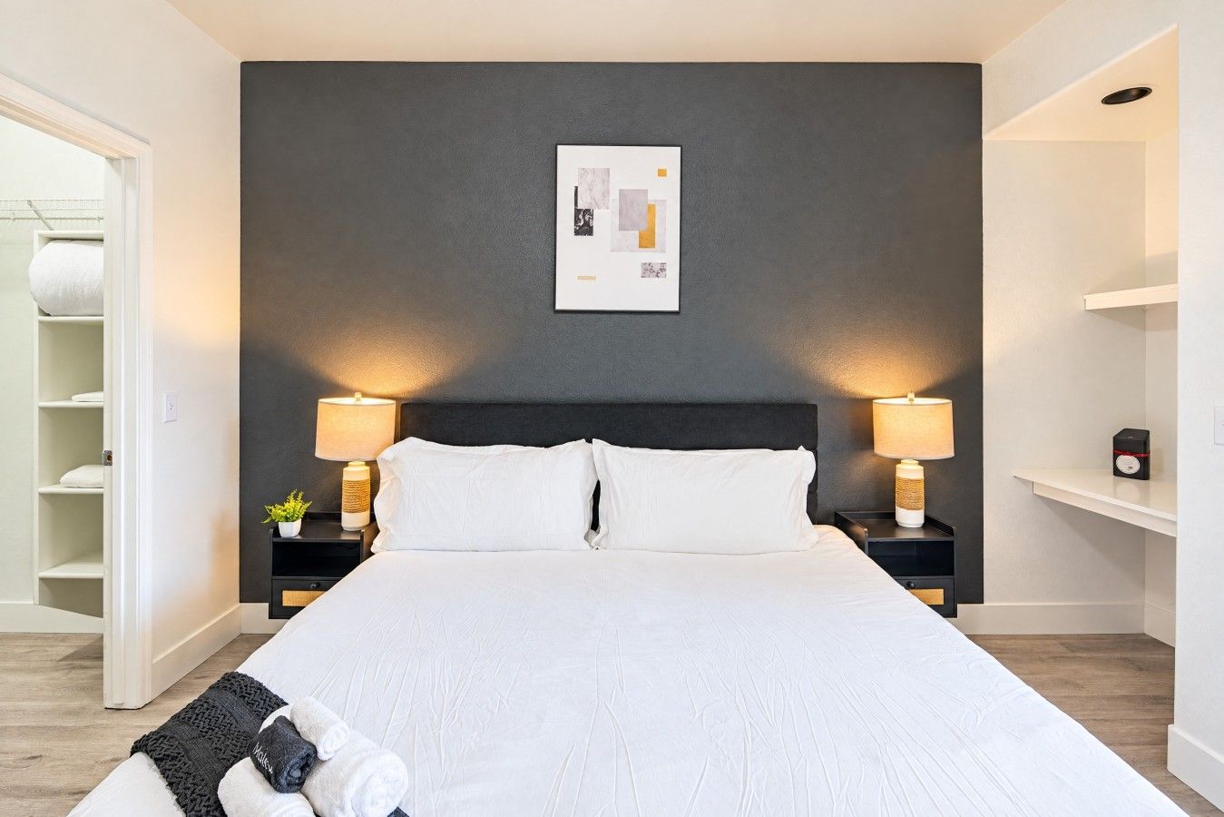 Une chambre d’hôtel avec un grand lit, deux tables de chevet avec des lampes, un mur d’accent de couleur sombre et une œuvre d’art encadrée au-dessus du lit.
