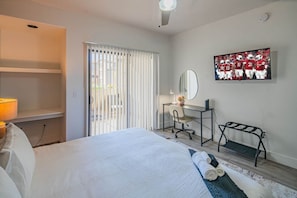 A hotel room with a bed, a desk with a chair, a TV, and a window with blinds.