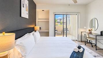 A hotel room with a bed, a desk, a chair, a lamp, a ceiling fan, and a view of the outside.