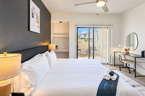 Habitación de hotel con cama, escritorio, silla, lámpara, ventilador de techo y vistas al exterior.
