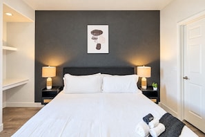 Un cuarto de hotel con una cama grande, dos mesitas de noche con lámparas, una obra de arte enmarcada en la pared y una puerta.