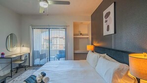 Habitación de hotel con una cama grande, un escritorio con silla, un espejo, ventilador de techo y vista por la ventana.