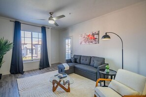 Un salon moderne avec un canapé gris, un fauteuil blanc, une table basse en verre et un lampadaire.