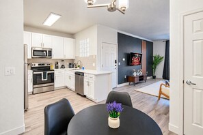 Una cocina moderna con armarios blancos, electrodomésticos de acero inoxidable y un comedor con una mesa redonda y sillas.