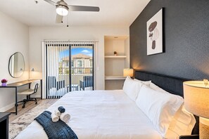 A hotel room with a bed, desk, chair, and a view of the outside.