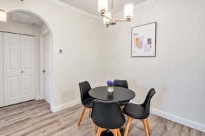 Una habitación con una mesa redonda, cuatro sillas, una araña y una obra de arte abstracta enmarcada en la pared.