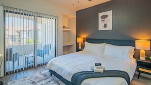 Habitación de hotel con una cama grande, un ventilador de techo, una puerta corrediza de vidrio al balcón y un cuadro en la pared.