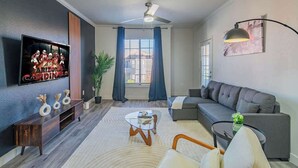 Una sala moderna con una televisión de pantalla plana, un ventilador de techo, un sofá, una mesa de centro y una planta en maceta.