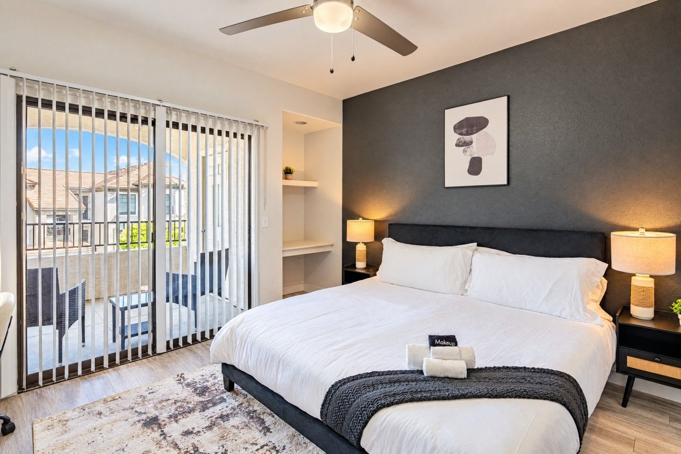 Une chambre avec un lit, un ventilateur de plafond, une table de chevet avec une lampe et une vue sur l’extérieur, accessible par une porte coulissante.
