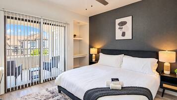Une chambre avec un lit, un ventilateur de plafond, une table de chevet avec une lampe et une vue sur l’extérieur, accessible par une porte coulissante.