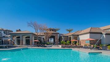 A swimming pool with lounge chairs and umbrellas, surrounded by buildings with a consistent architectural style.