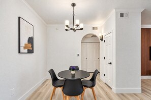 Een eetruimte met een ronde tafel, zwarte stoelen, een kroonluchter en een kunstwerk in een lijst aan de muur.
