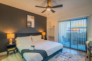 Ein Hotelzimmer mit Bett, Nachttischlampen, Deckenventilator, einem Fenster mit Jalousien und Blick ins Freie.