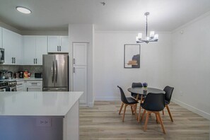 A modern kitchen with white cabinets, a stainless steel refrigerator, and a dining area with a round table and black chairs.