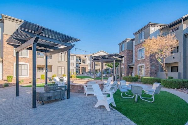 Un patio con mobiliario exterior, una pérgola y un pequeño hogar para la chimenea.