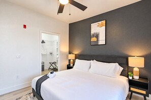 Een hotelkamer met een bed, nachtkastjes, een plafondventilator, een schilderij aan de muur en een kledingkast met kleren.