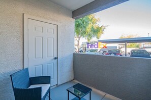 A balcony with a white door, a wicker chair, a small table, and a view of a FedEx truck in the background.