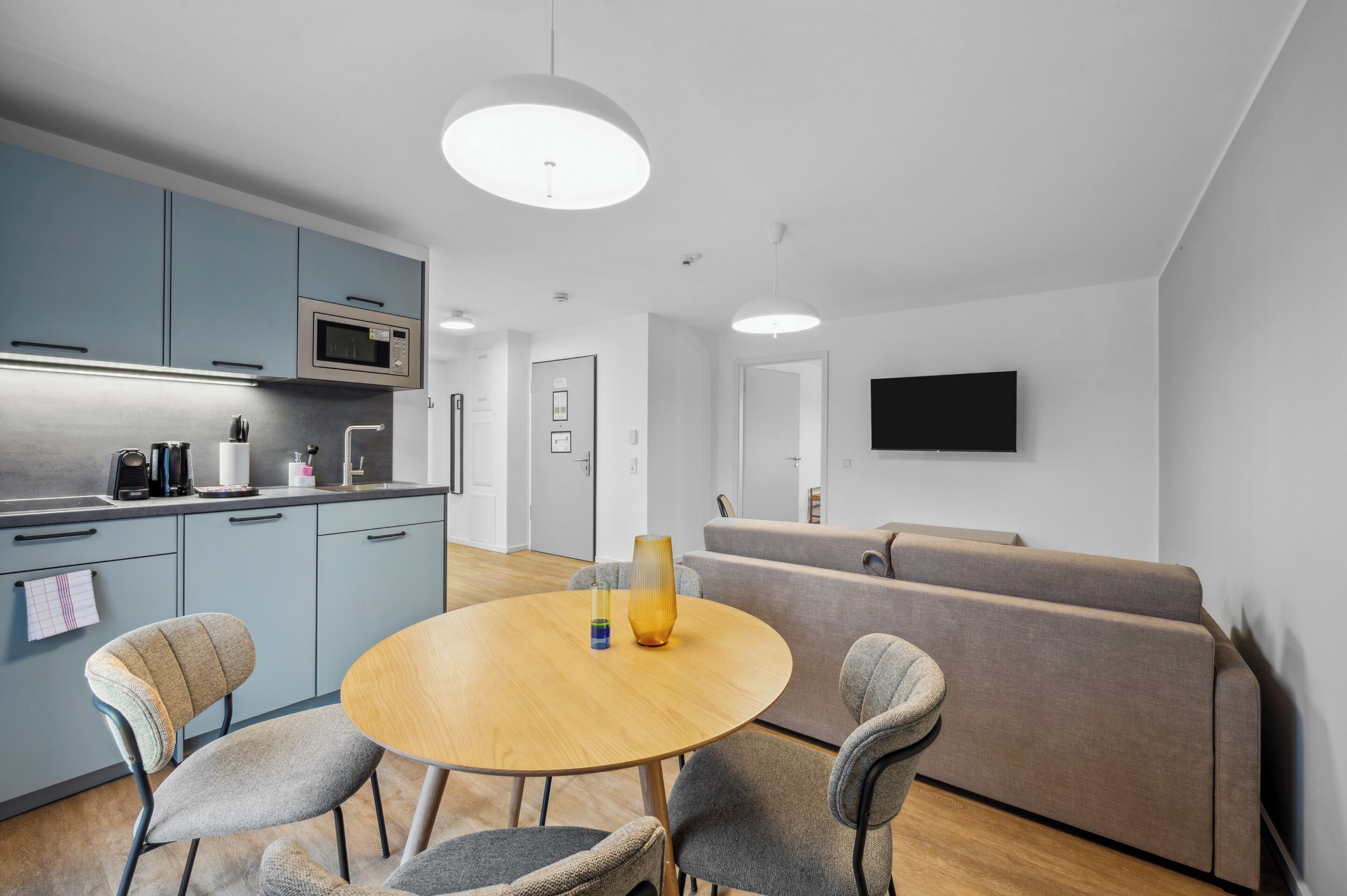 A modern kitchen with blue cabinets, a microwave, and a dining area with a round table and chairs.