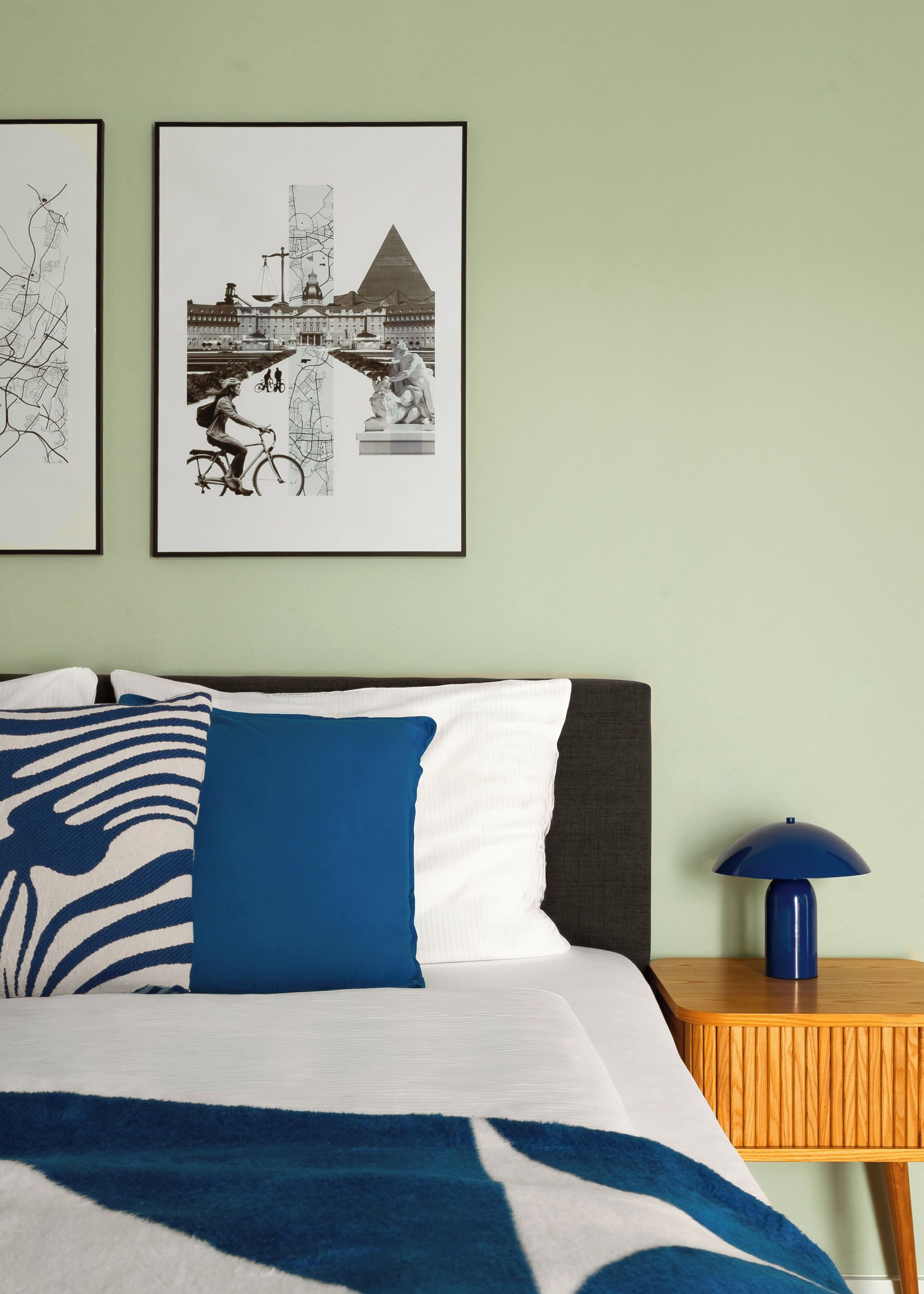 A neatly made bed with a patterned blanket, a blue pillow, and a framed picture of a cityscape on the wall.