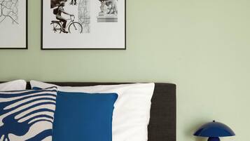 A neatly made bed with a patterned blanket, a blue pillow, and a framed picture of a cityscape on the wall.