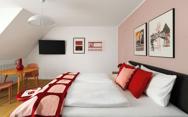 Une chambre à coucher moderne avec un lit, un bureau, une chaise, un vase rouge et des tableaux encadrés accrochés au mur.