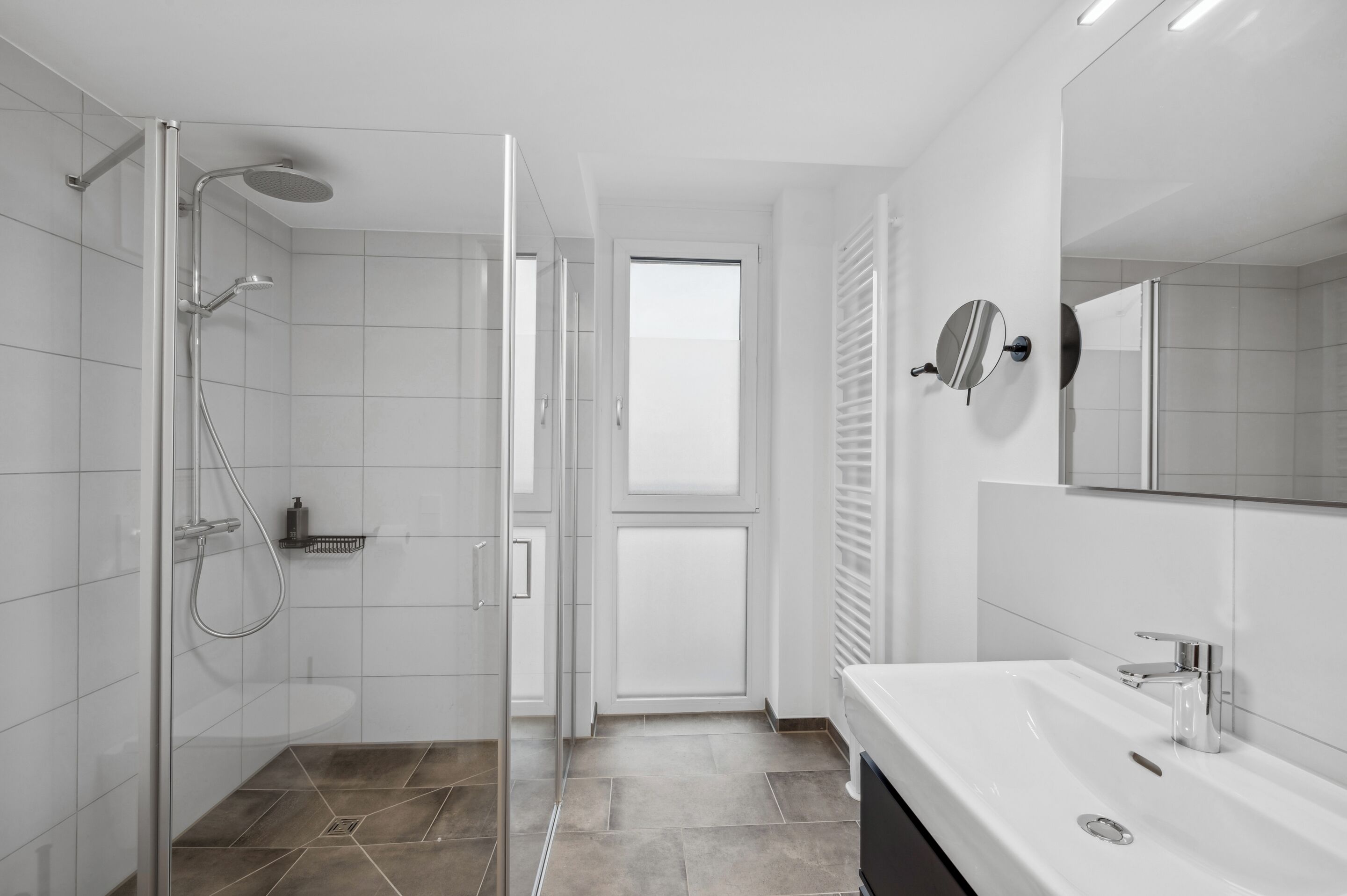 A modern bathroom with a glass shower enclosure, a white sink, and a large mirror.