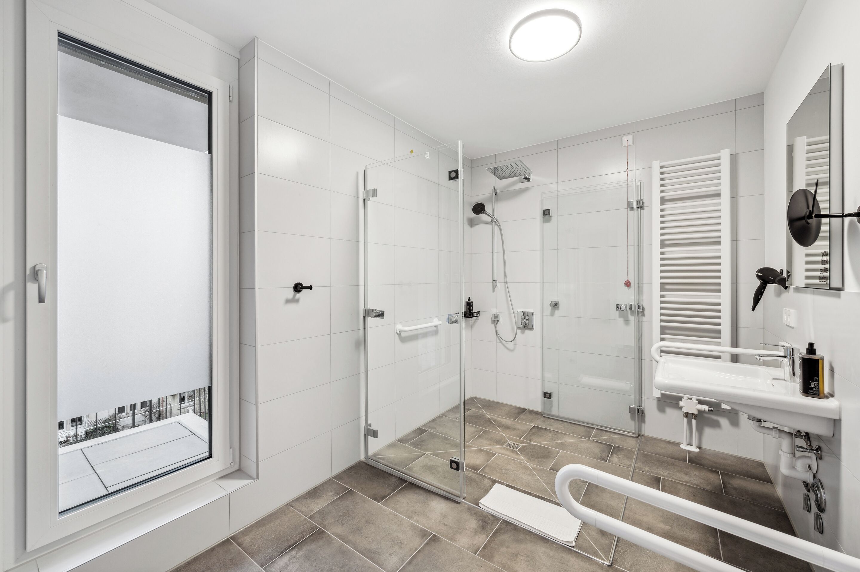 Un baño moderno con cabina de ducha de vidrio, un lavabo blanco y un ventanal con vistas.