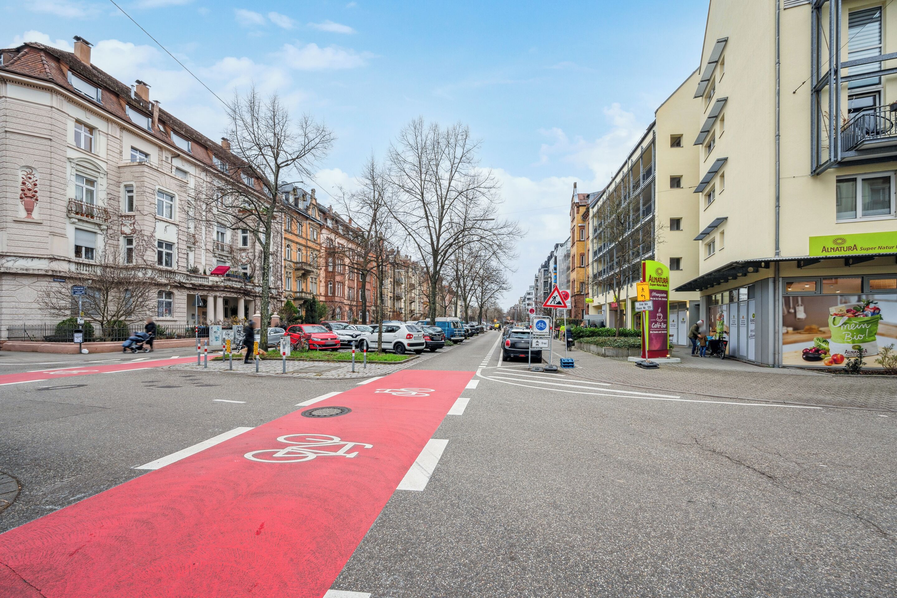 Ruas com faixa vermelha para bicicletas, carros estacionados e edifícios com sacadas.