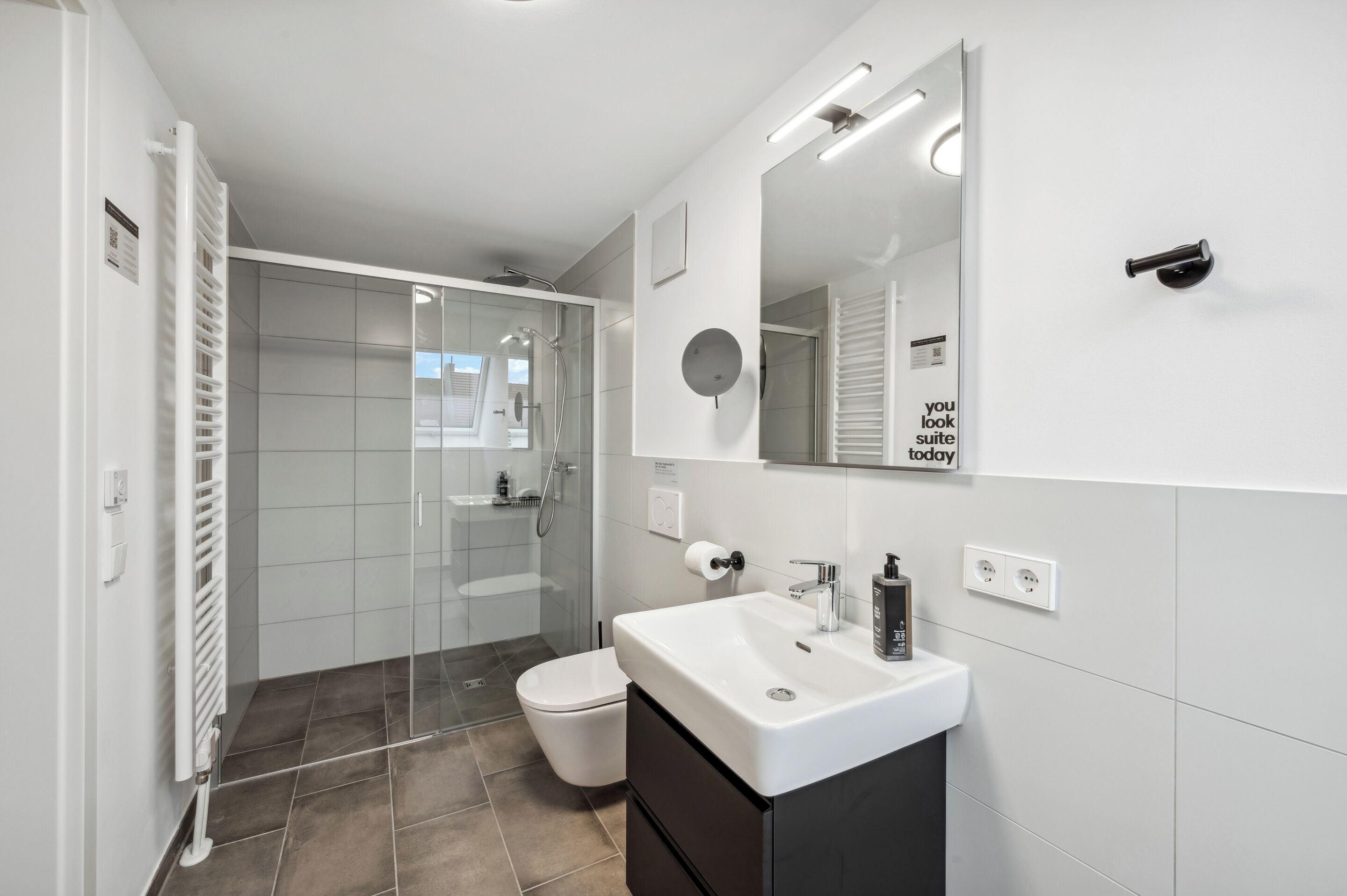 A modern bathroom with a glass shower enclosure, a white sink, and a large mirror.