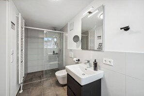 Une salle de bain moderne avec une douche à l’italienne en verre, un lavabo blanc et un grand miroir.