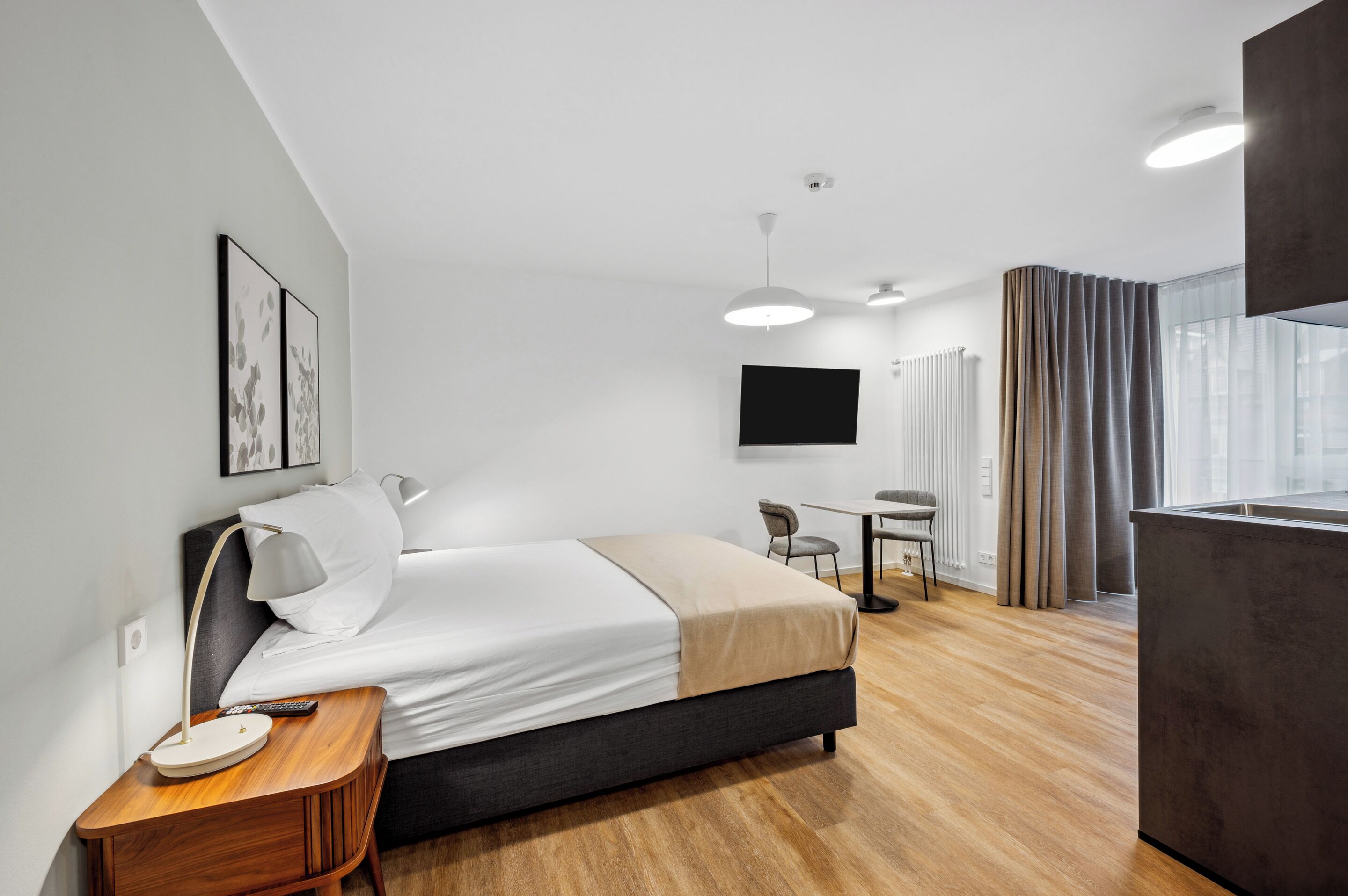 A modern hotel room with a bed, bedside table, lamp, and a flat-screen TV mounted on the wall.