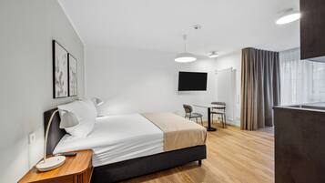 A modern hotel room with a bed, bedside table, lamp, and a flat-screen TV mounted on the wall.