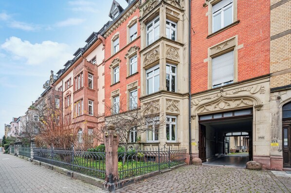 A historic building with ornate architectural details, a cobblestone street, and a metal fence.
