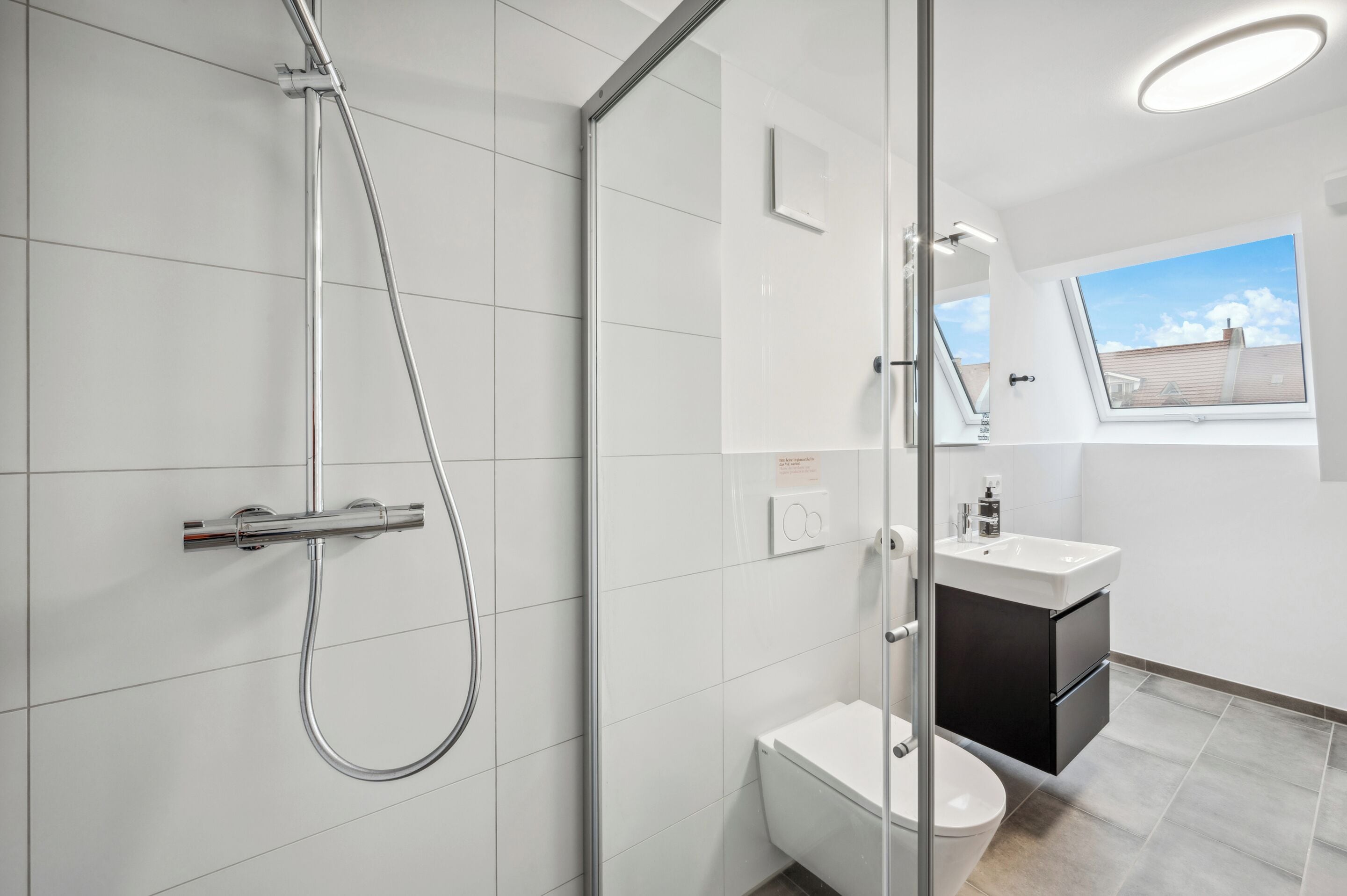 Une salle de bain moderne dotée d’une douche à parois de verre, de toilettes et d’un lavabo avec un meuble noir.