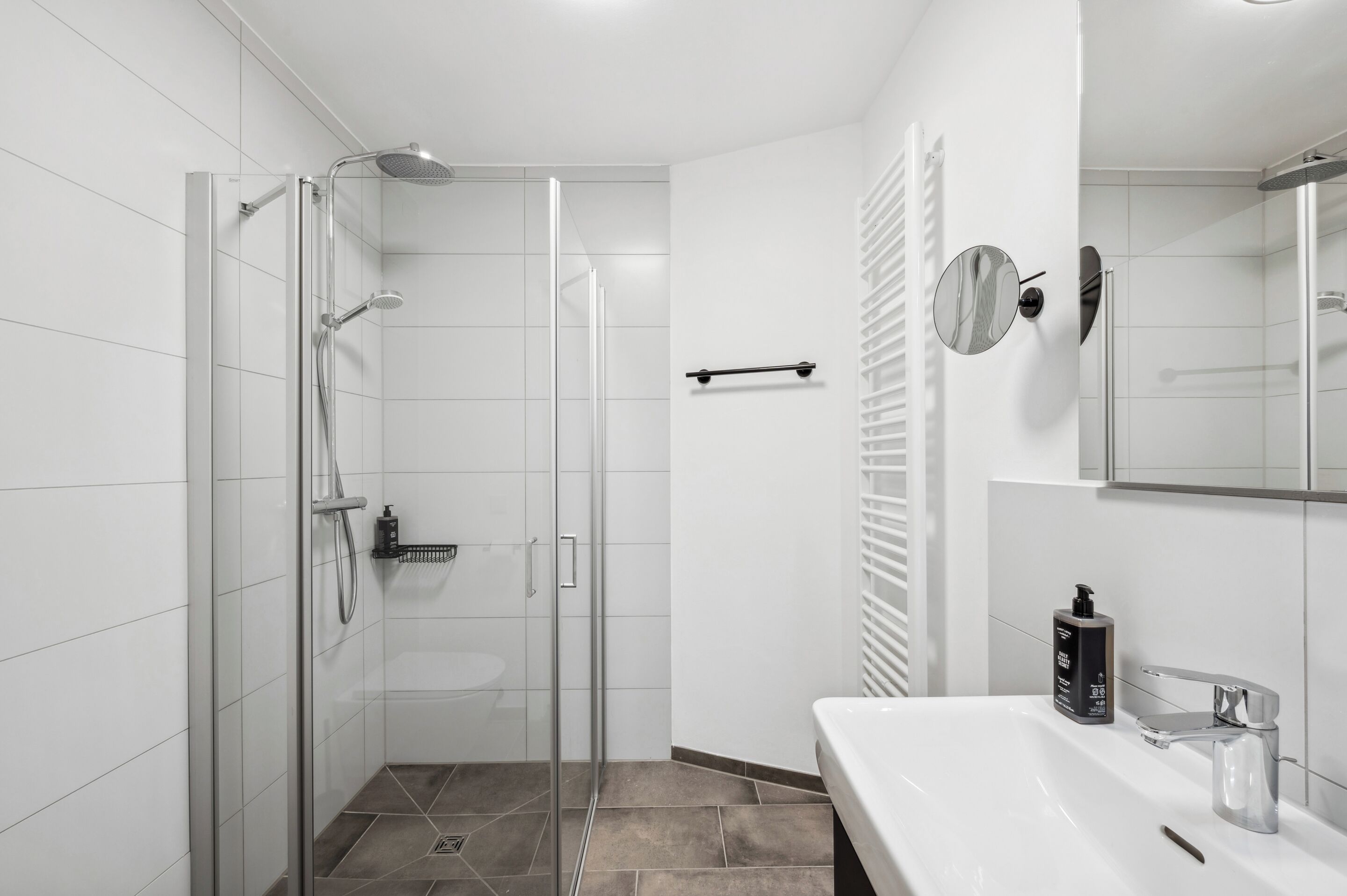 Une salle de bain moderne avec une douche à parois de verre, un lavabo blanc et un miroir.