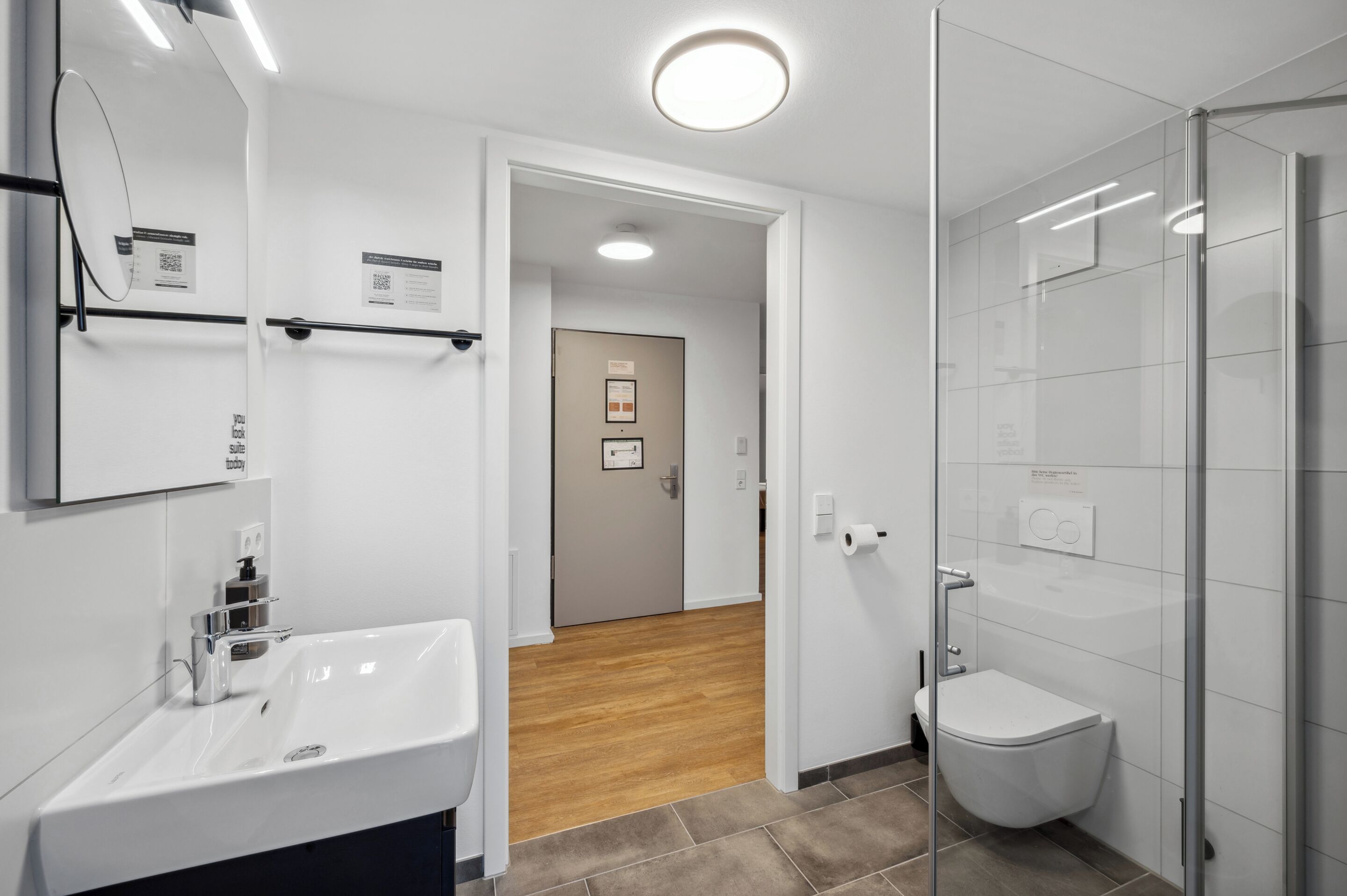 Une salle de bain moderne avec un lavabo blanc, une douche en verre et un plancher en bois.