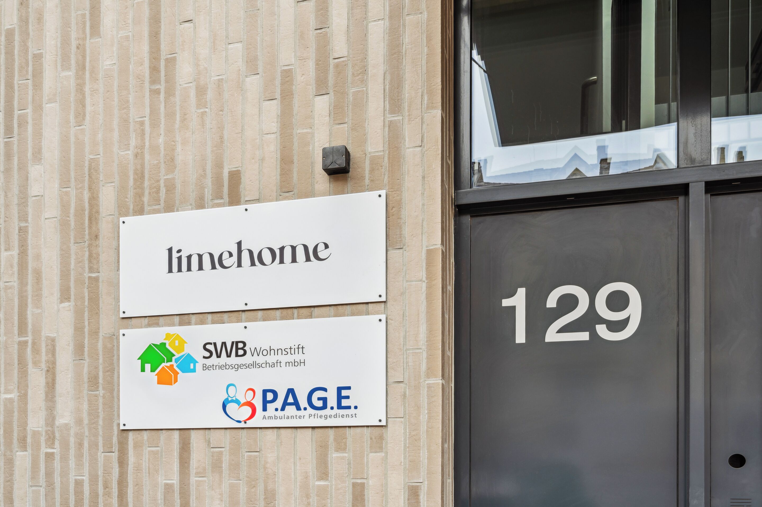 Ein Gebäude mit einem Schild, auf dem "limhome" steht, sowie einem Schild für "SWB Wohnstift Betriebsgesellschaft mbH" und dem Logo von "P.A.G.E. Ambulanten Pflegedienst".