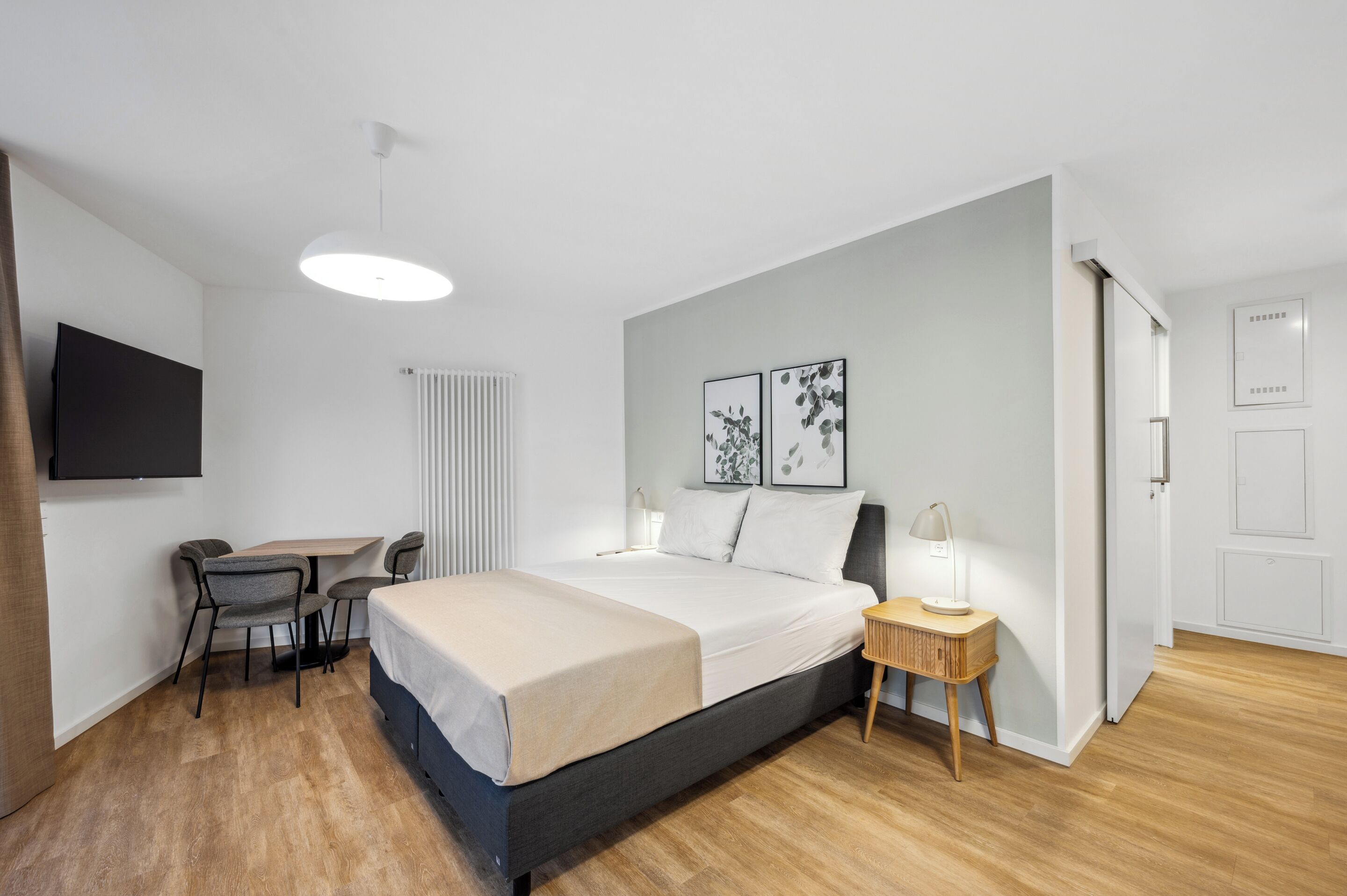 A modern bedroom with a bed, bedside table, lamp, and a desk with a chair.